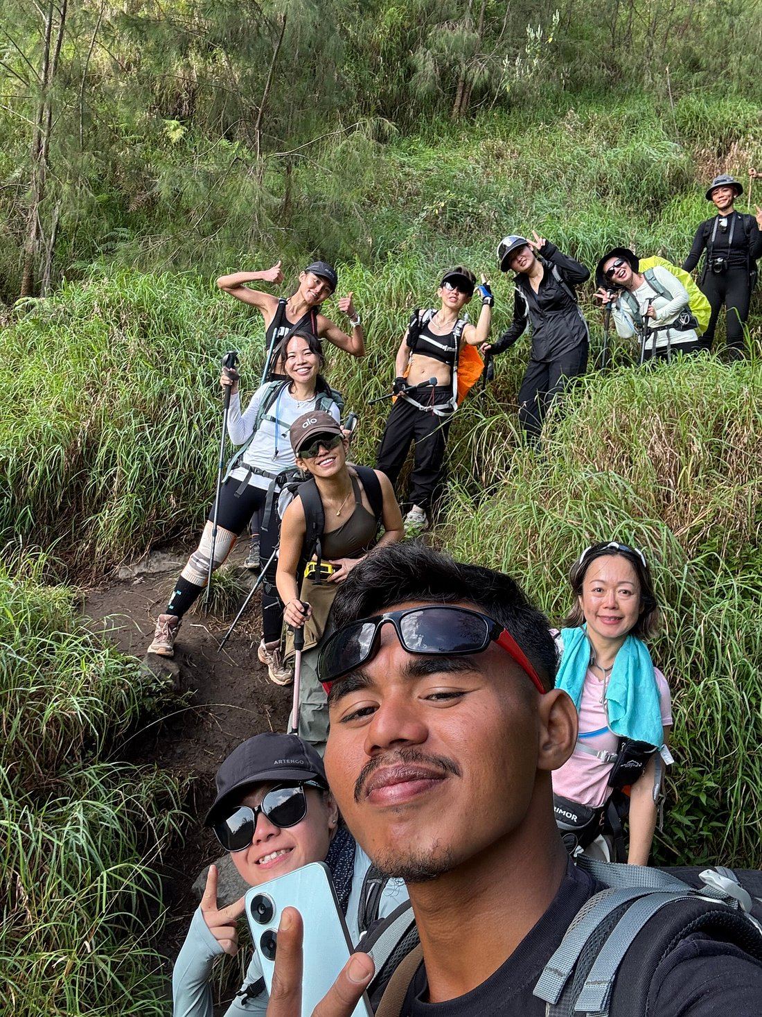 A guide takes a selfie with his group on a green, overgrown stretch of the Rinjani trail