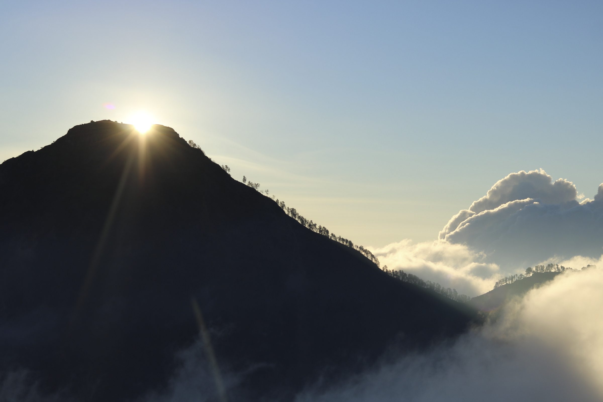 The sun rising behind the Mount Rinjani crater rim, with cloud filling the valley below the ridge