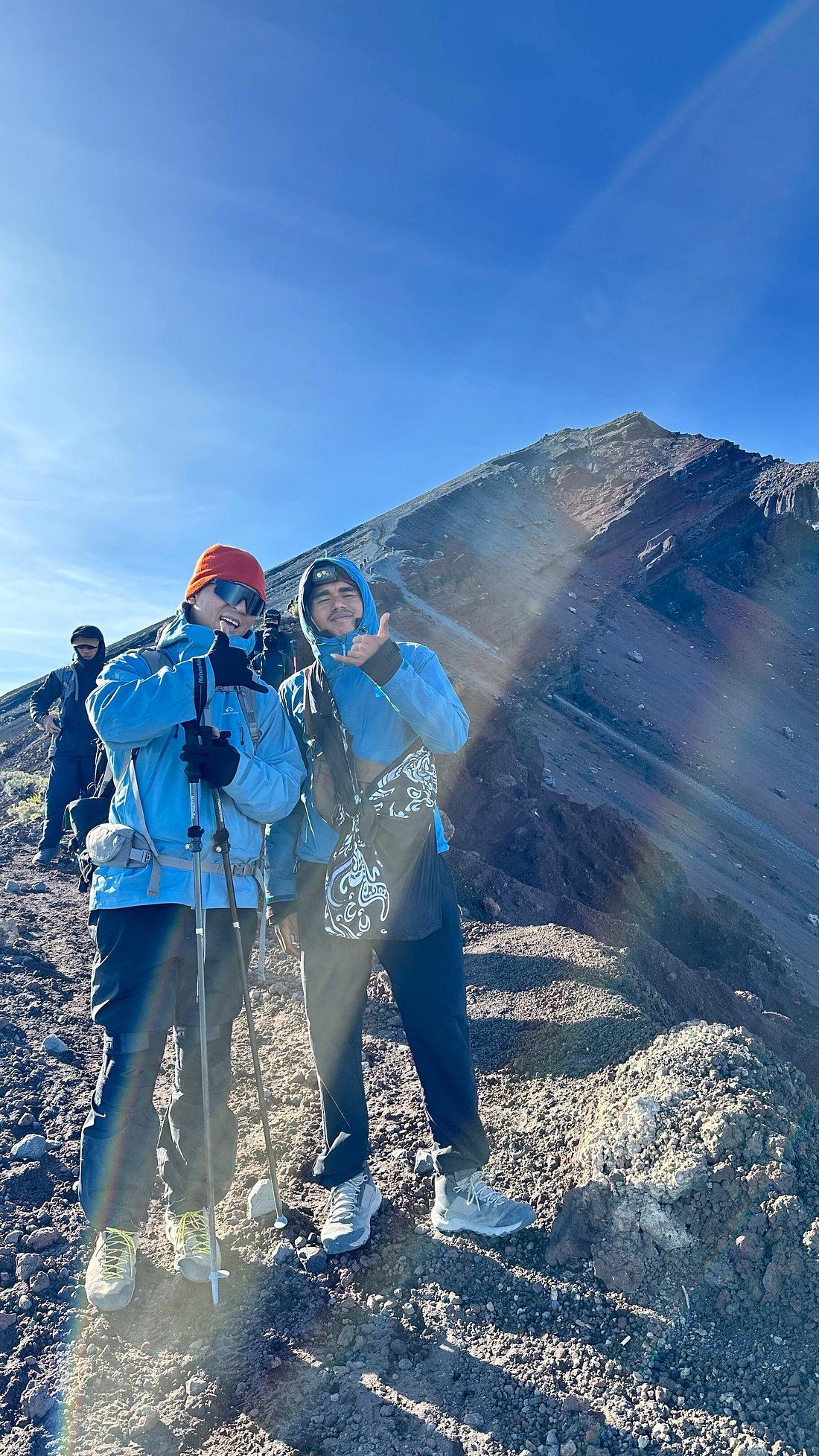Two trekkers on the volcanic scree slope near Rinjani's summit in early morning light