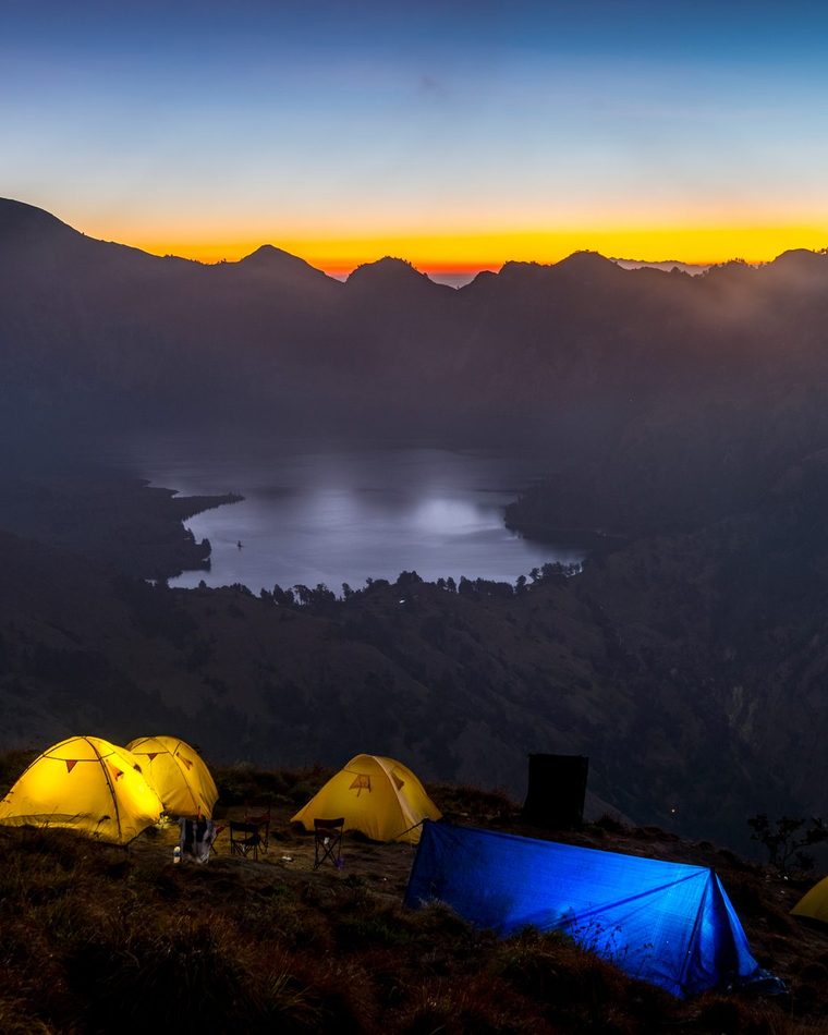 Mount Rinjani crater rim camp at sunset with glowing tents and volcanic landscape