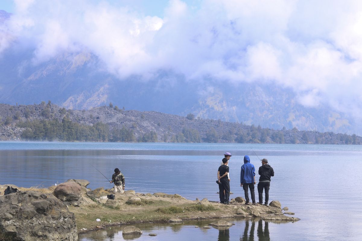 Four trekkers standing on the shore of Segara Anak, the crater lake, with the caldera wall in cloud behind them